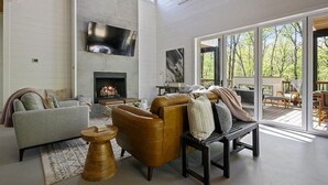 Amplia sala de estar con chimenea, televisor grande y vistas al exterior a través de amplias puertas corredizas de vidrio.