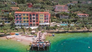 Un hotel de varios pisos con piscina, rodeado de follaje y un frente marítimo de aguas cristalinas.