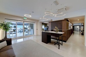 Un espace de bureau moderne comprenant un comptoir d’accueil, une grande plante et une porte vitrée donnant sur un espace extérieur.