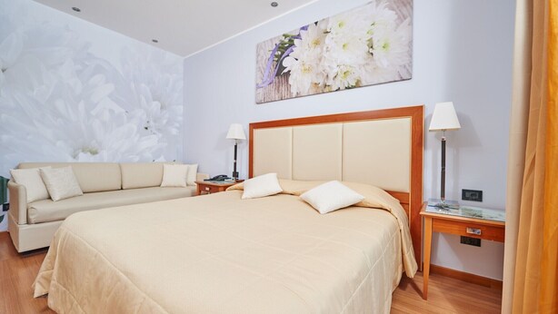 Una habitación de hotel con una cama grande, un sofá, dos mesitas de noche con lámparas y una obra de arte floral en la pared.