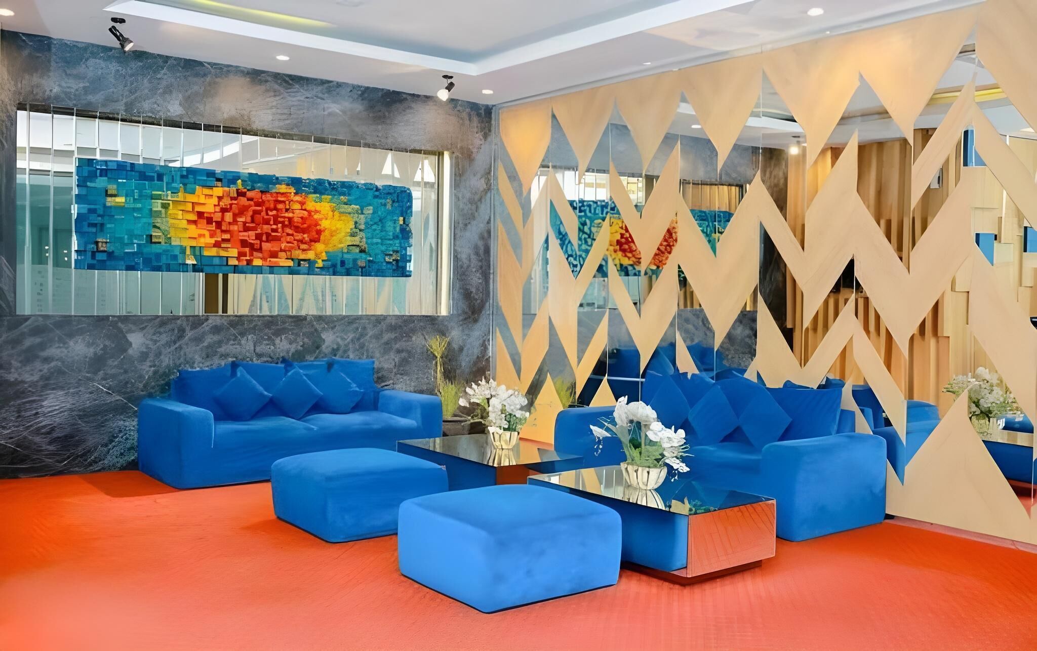 Eine moderne Lobby mit blauen Sofas, farbenfroher abstrakter Wandkunst und einer geometrisch gemusterten Trennwand.