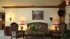 A traditional living room with a patterned floor, a sofa, two armchairs, a coffee table, and wall-mounted lamps. - Hotel Restaurant Hoettche (Dormagen)