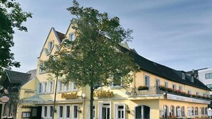 A yellow building with a balcony and a tree in front. - Hotel Restaurant Hoettche (Dormagen)