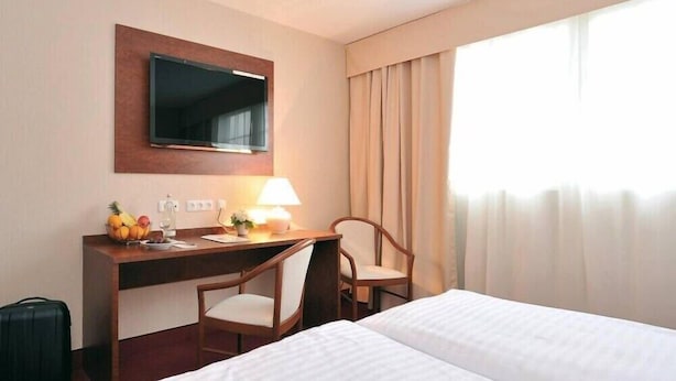 A hotel room with a bed, desk, chair, television, and curtains. - Hotel Restaurant Hoettche (Dormagen)