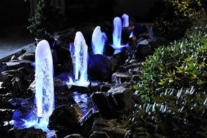 Un jardín nocturno con fuentes iluminadas y rocas.