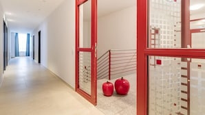 A hallway with a red-framed door, a staircase, and two red apples on the floor.