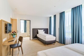 A hotel room with a bed, a desk with a chair, a TV, and a window with curtains. - Hotel Apfelrot (Erding)
