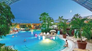 An indoor swimming pool with lounge chairs and palm trees.