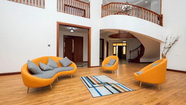 A spacious living area with two orange armchairs, a wooden floor, and a staircase leading to an upper level. - Tamarind Guesthouse and Suites (Accra)