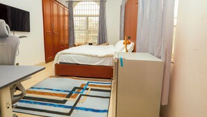 A bedroom with a bed, a desk, a chair, a TV, and a window with curtains. - Tamarind Guesthouse and Suites (Accra)