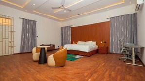 A modern bedroom with a wooden floor, a bed, a desk, a chair, and a ceiling fan. - Tamarind Guesthouse and Suites (Accra)