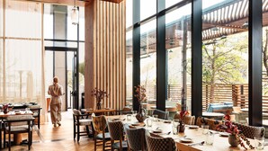 A modern dining area with wooden flooring, large windows, and a view of the outdoors.