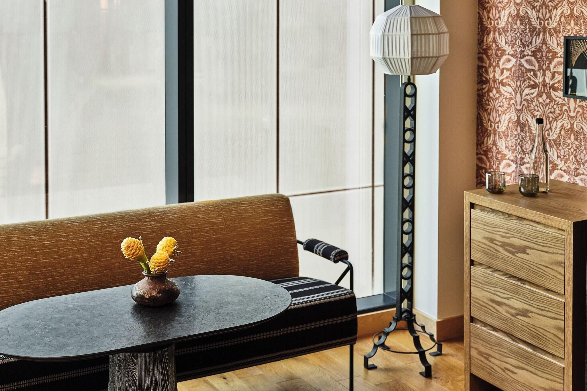 A modern interior with a round table, a wooden bench, a floor lamp, and a patterned wall.