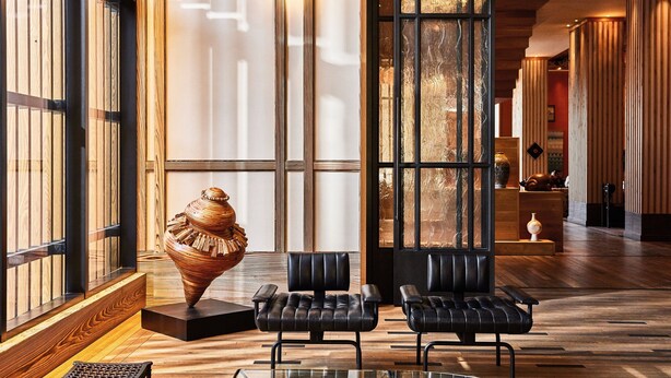 A lobby with wooden flooring, black leather chairs, a glass table, and a large vase sculpture.
