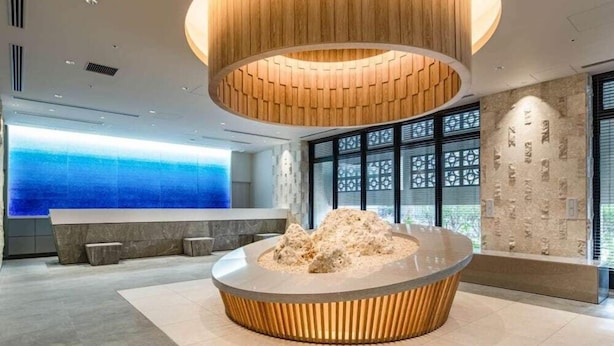 A modern lobby with a circular seating area, a large wooden ceiling structure, and a view of the ocean through large windows. - Okinawa Hinode Resort And Hot Spring Hotel (Naha)