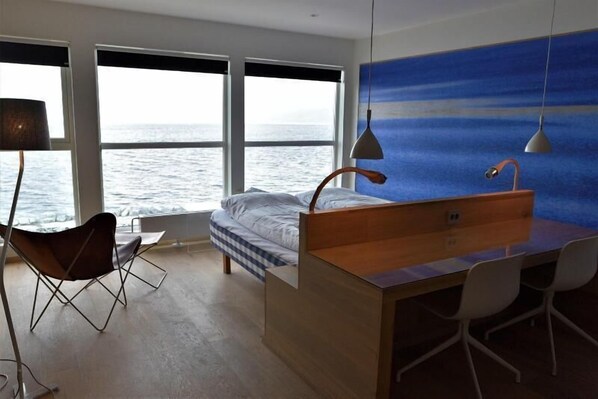 A modern room with a large window overlooking the sea, a bed, a desk with chairs, and a pendant light. - Malangen Resort (Balsfjord)