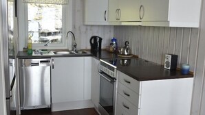 Una cocina compacta con armarios blancos, horno integrado, lavaplatos y fregadero.