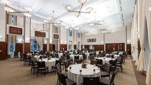 Une vaste salle de banquet avec des tables rondes, des chaises et des lustres au plafond.