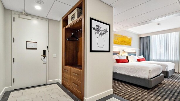 Une chambre d’hôtel avec un lit, une armoire, un tableau encadré et une fenêtre avec des rideaux.