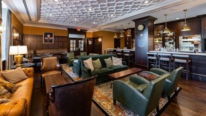 Un hall d’entrée avec des canapés en cuir, une table basse, un tapis à motifs, un coin bar avec des tabourets et une horloge au mur.