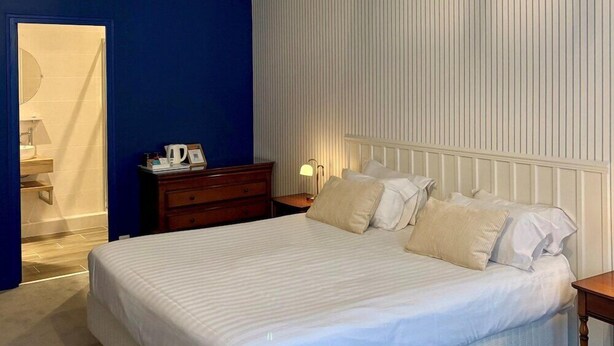 A bedroom with a large bed, a wooden nightstand, a bedside table with a lamp, and a bathroom visible through an open door. - Hotel Restaurant de la Marine (Saint-Herblain)