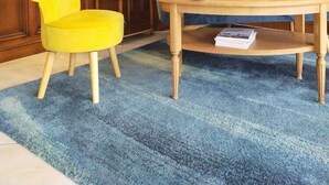 A room with teal walls, a wooden paneled ceiling, a blue upholstered sofa, a yellow chair, a wooden table with a lamp, and a framed picture on the wall. - Hotel Restaurant de la Marine (Saint-Herblain)