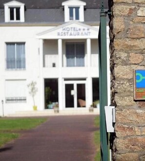 Un hôtel avec une enseigne indiquant « HÔTEL RESTAURANT » et une enseigne verte avec un symbole bleu sur la droite.