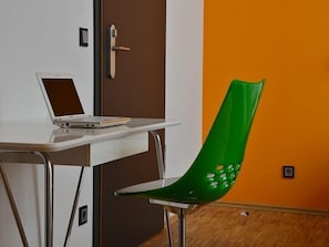 Una habitación con un escritorio blanco, una computadora portátil, una silla verde, una puerta y una pared naranja.