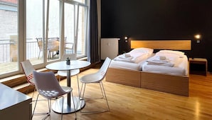 A modern hotel room with a large bed, a small round table, two chairs, and a view of the outside through large windows. - Say Cheese Leipzig Hotel and Hostel (Leipzig)