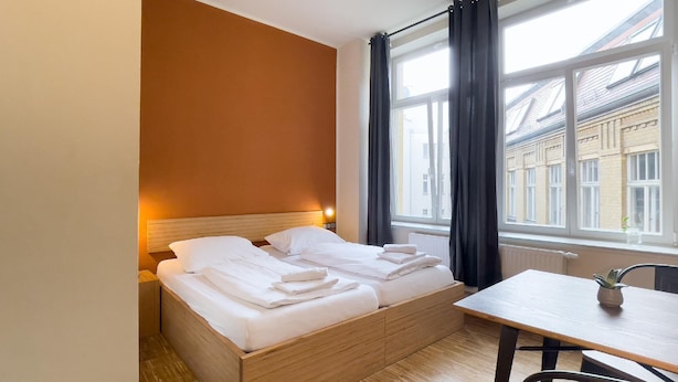 A hotel room with a wooden bed, a small table, and a view of buildings through the window. - Say Cheese Leipzig Hotel and Hostel (Leipzig)