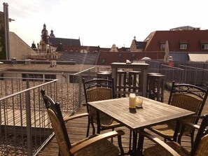 An outdoor seating area with tables and chairs, a view of buildings in the background, and a railing. - Say Cheese Leipzig Hotel and Hostel (Leipzig)