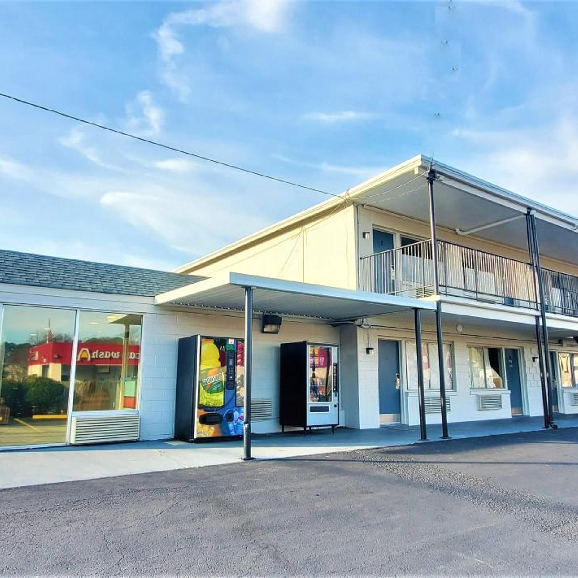 A two-story building with a flat roof, a balcony on the upper floor, and a storefront with a vending machine.