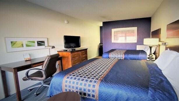 A hotel room with a desk, two beds, a television, and a window with a view of a building. - Travelodge Newport News (Newport News)