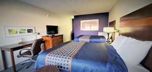 Une chambre d’hôtel équipée d’un bureau, de deux lits, d’une télévision et d’une fenêtre donnant sur un immeuble.