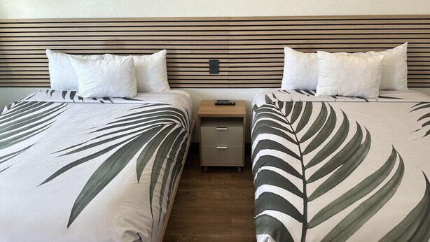 A hotel room with two beds, each with a leaf-patterned bedspread, a wooden headboard, and a nightstand with a drawer. - Swai Hotel (Lake Havasu City)
