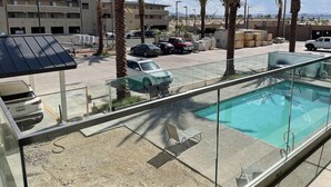 A pool area with clear glass barriers, a few lounge chairs, and palm trees. - Swai Hotel (Lake Havasu City)