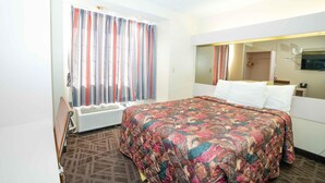 A hotel room with a large bed, a window with striped curtains, a mirror, and a radiator. - Regency Inn & Suites DFW (Euless)