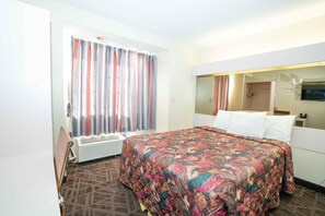 A hotel room with a large bed, a window with striped curtains, a mirror, and a radiator. - Regency Inn & Suites DFW (Euless)