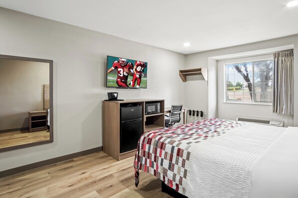 A hotel room with a bed, a desk, a TV, a mirror, and a window with curtains. - Regency Inn & Suites DFW (Euless)