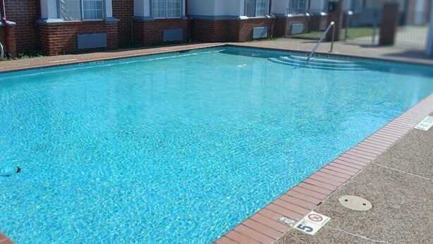 A rectangular swimming pool with clear blue water, surrounded by a brick wall and a tiled deck.