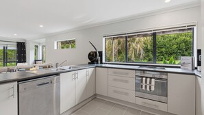 A modern kitchen with a dishwasher, oven, and sink. There is a window with a view of greenery.