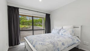 A bedroom with a bed, a window with curtains, and a view of greenery outside.