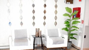 A living room with two white armchairs, a patterned rug, a potted plant, and decorative wall sconces. - Days Inn Attleboro (Attleboro)
