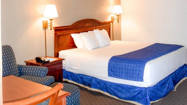 A hotel room with a bed, two bedside lamps, a desk, a chair, and a small table. - Days Inn Attleboro (Attleboro)