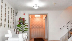 A modern living room with a white sofa set, a potted plant, and a patterned rug. - Days Inn Attleboro (Attleboro)