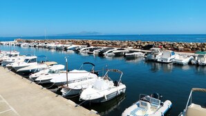 Un puerto deportivo con varias embarcaciones amarradas, un rompeolas rocoso y un cielo azul despejado.