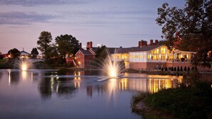 A lakeside hotel with a reflection of its lights on the water, surrounded by trees and other buildings. - Nationwide Hotel And Conference Center (Lewis Center)