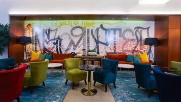 A lobby with colorful chairs, a round table, and a large abstract mural on the wall.
