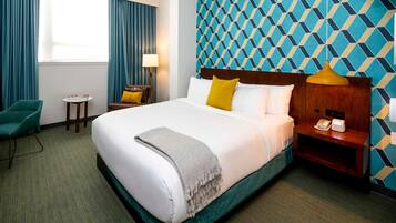 A hotel room with a large bed, a desk, a chair, a lamp, and a patterned wall.