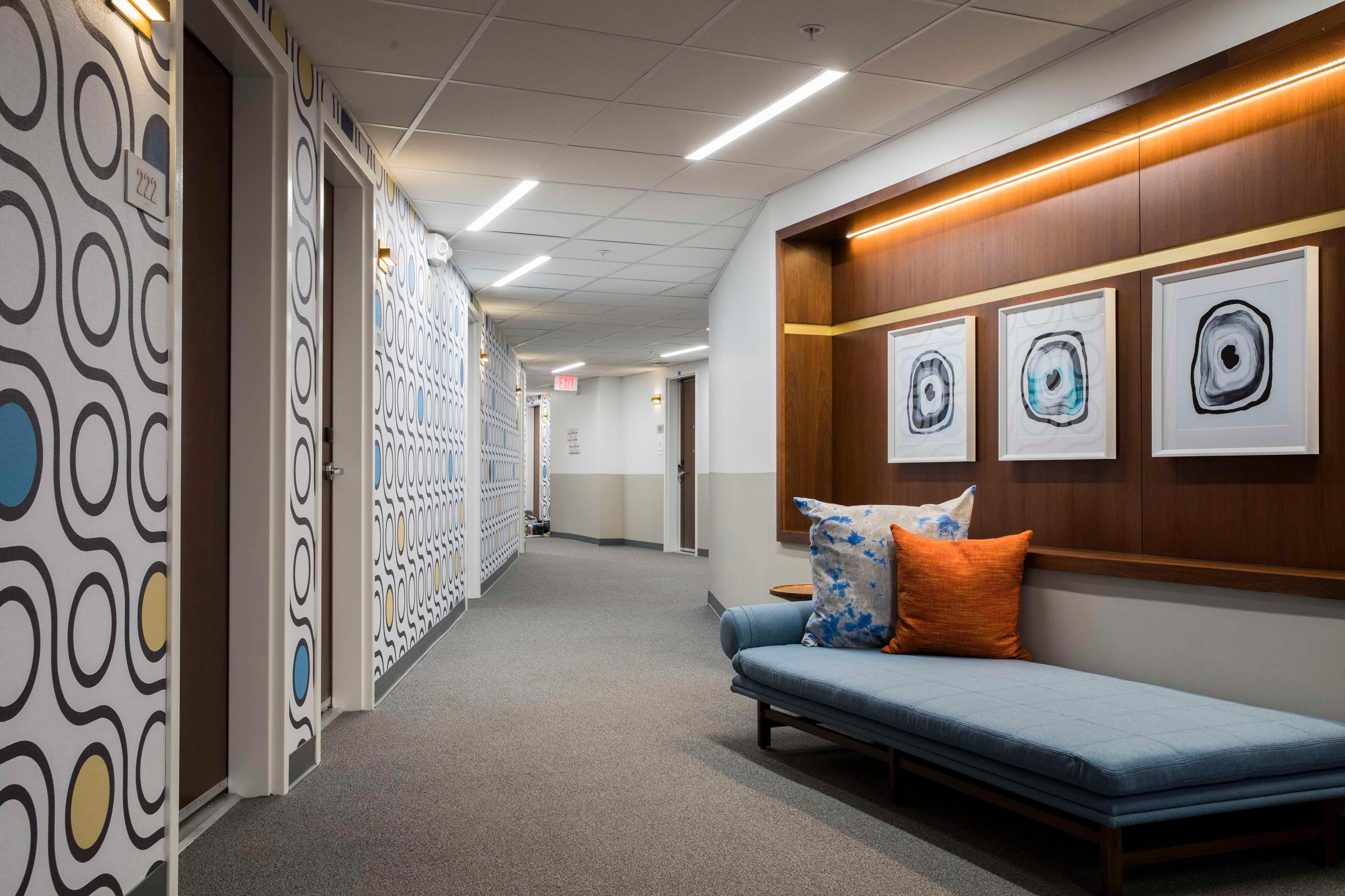 A hallway with patterned walls, a blue sofa with pillows, and framed artwork on the wall.